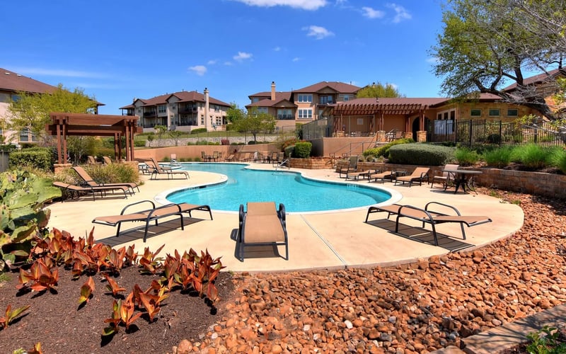 Resort swimming pool with lounge chairs, surrounded by desert landscaping and residential buildings under blue sky